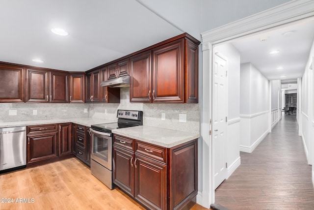 kitchen with decorative backsplash, light stone countertops, stainless steel appliances, and light hardwood / wood-style flooring