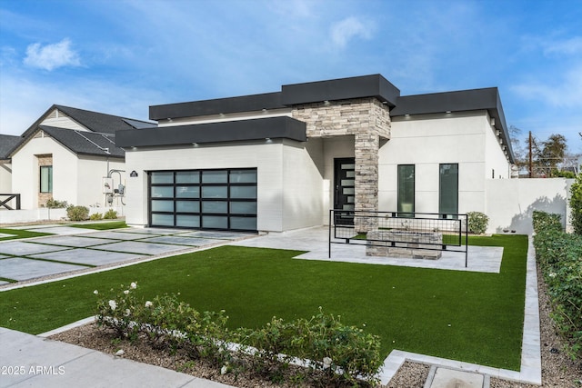 modern home with an attached garage, fence, stone siding, driveway, and a front lawn