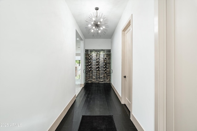 corridor with dark wood-style floors, a chandelier, and baseboards