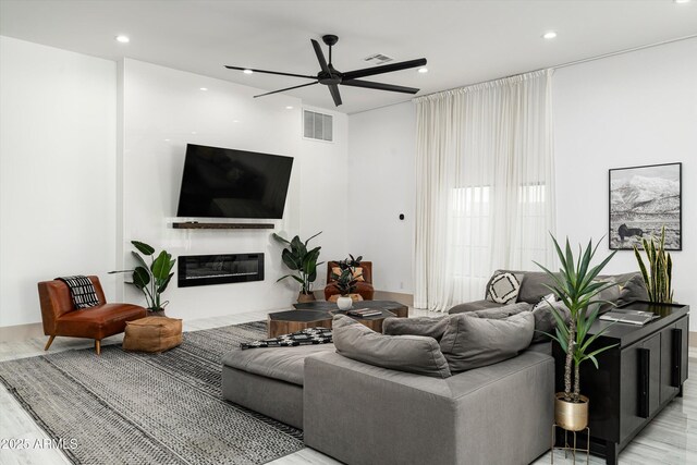 living area with a glass covered fireplace, visible vents, ceiling fan, and recessed lighting