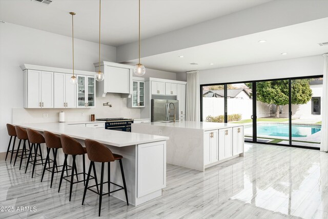 kitchen featuring built in fridge, white cabinets, light countertops, a kitchen bar, and gas stove