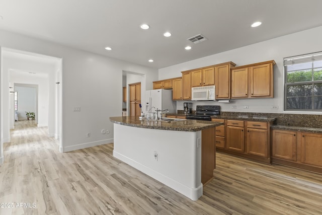 kitchen with white appliances, visible vents, brown cabinets, a kitchen island with sink, and recessed lighting