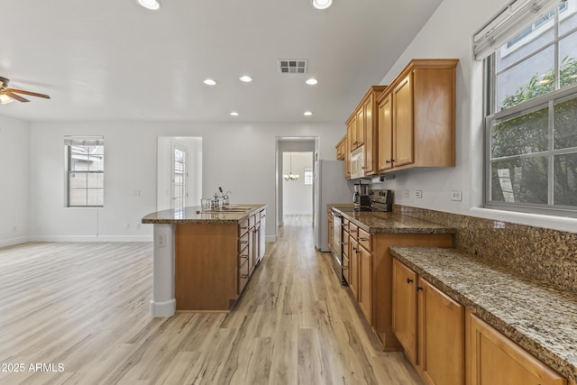 kitchen featuring light wood finished floors, a kitchen island with sink, white appliances, and visible vents