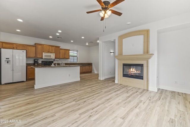 kitchen with brown cabinetry, open floor plan, light wood-type flooring, a tile fireplace, and white appliances