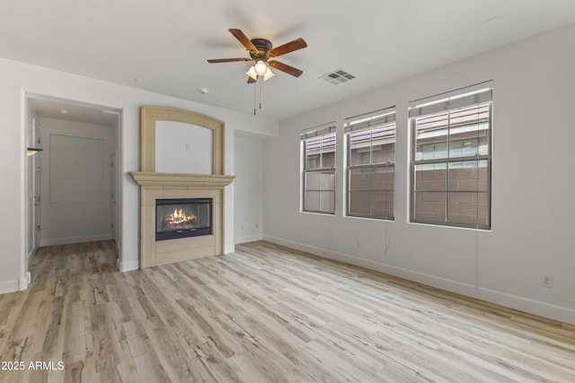 unfurnished living room featuring plenty of natural light, light wood-style flooring, visible vents, and a tile fireplace