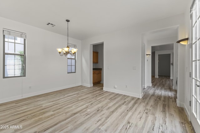 empty room with baseboards, visible vents, light wood finished floors, and an inviting chandelier