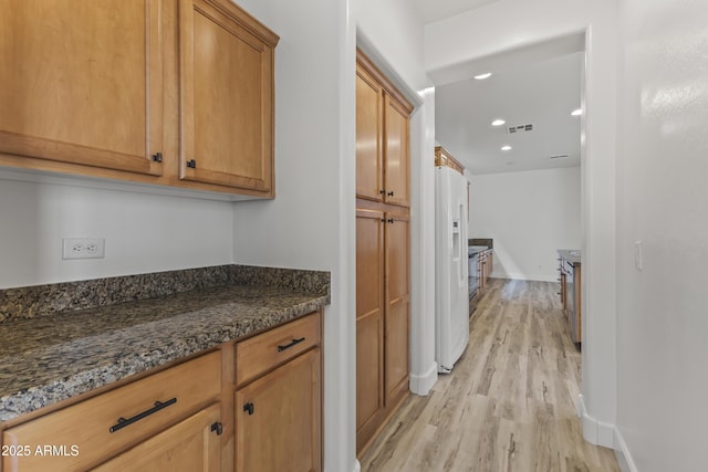 kitchen featuring white fridge with ice dispenser, dark stone countertops, light wood-style flooring, and baseboards