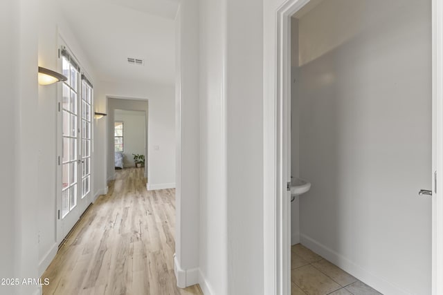 corridor featuring light wood-type flooring, baseboards, and visible vents