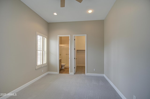 unfurnished bedroom with baseboards, light colored carpet, ensuite bath, a walk in closet, and recessed lighting