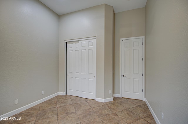 unfurnished bedroom with light tile patterned floors, a closet, and baseboards