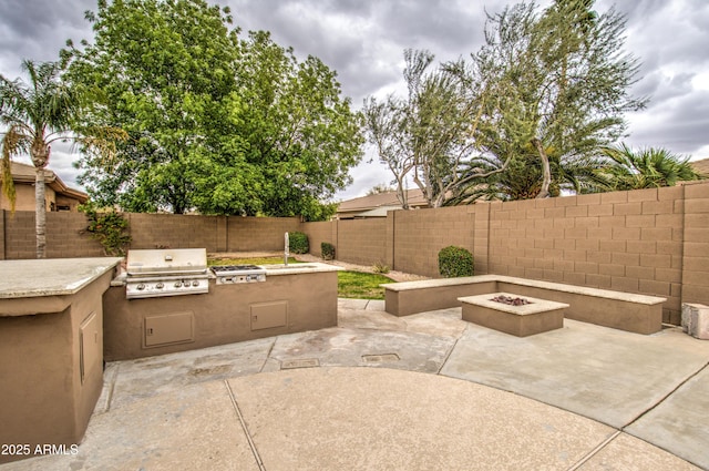 view of patio featuring a fenced backyard, a fire pit, an outdoor kitchen, and area for grilling