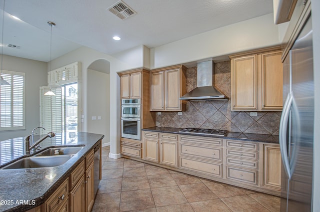 kitchen with visible vents, appliances with stainless steel finishes, a sink, wall chimney range hood, and backsplash