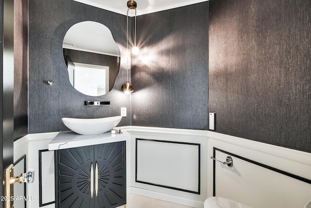 bathroom featuring a wainscoted wall, a sink, and a decorative wall