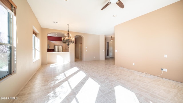 unfurnished living room with ceiling fan with notable chandelier, light tile patterned flooring, and a wealth of natural light