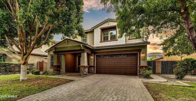 craftsman-style home featuring decorative driveway, stone siding, an attached garage, and fence