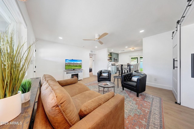 living area with light wood-style floors, ceiling fan, recessed lighting, and a barn door