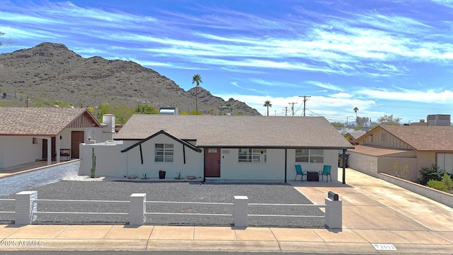 ranch-style house featuring a mountain view, a fenced front yard, covered porch, and stucco siding