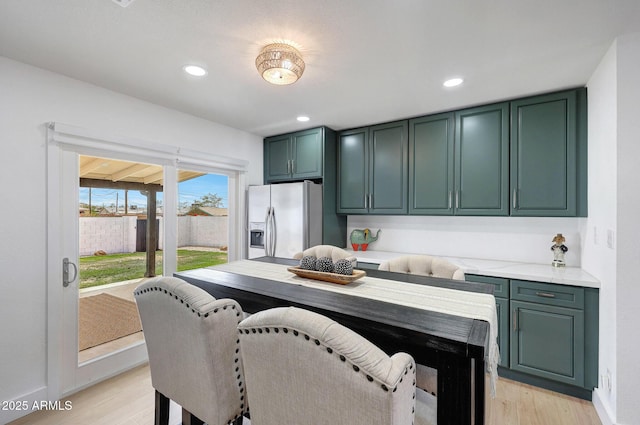 kitchen featuring recessed lighting, stainless steel fridge, green cabinets, light wood-type flooring, and baseboards