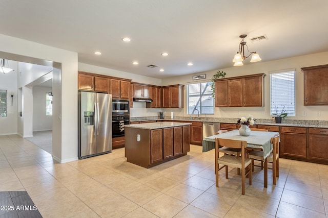 kitchen with light stone counters, recessed lighting, stainless steel appliances, under cabinet range hood, and a center island