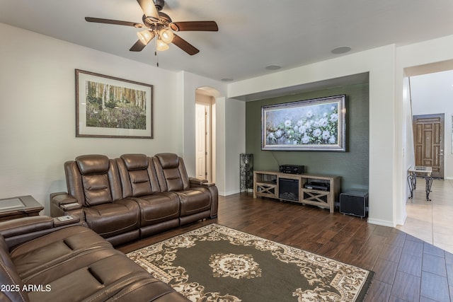 living area featuring baseboards, arched walkways, dark wood-type flooring, and ceiling fan