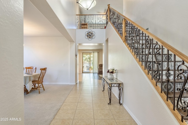 carpeted foyer with tile patterned flooring, a high ceiling, stairway, and baseboards