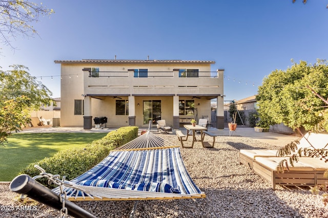 back of house featuring stucco siding, a ceiling fan, a patio, fence, and a balcony