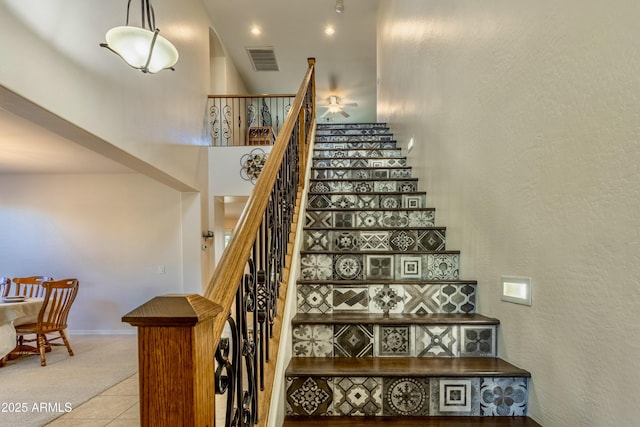 stairway with tile patterned floors, visible vents, carpet, baseboards, and a textured wall