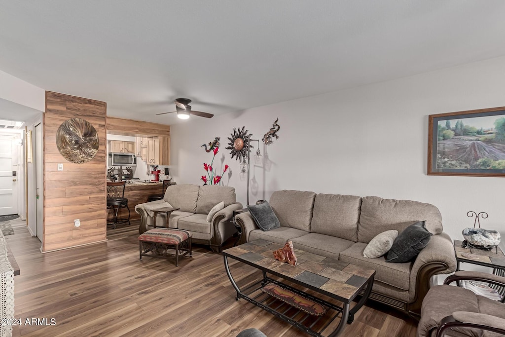 living room featuring ceiling fan, wood-type flooring, and wood walls