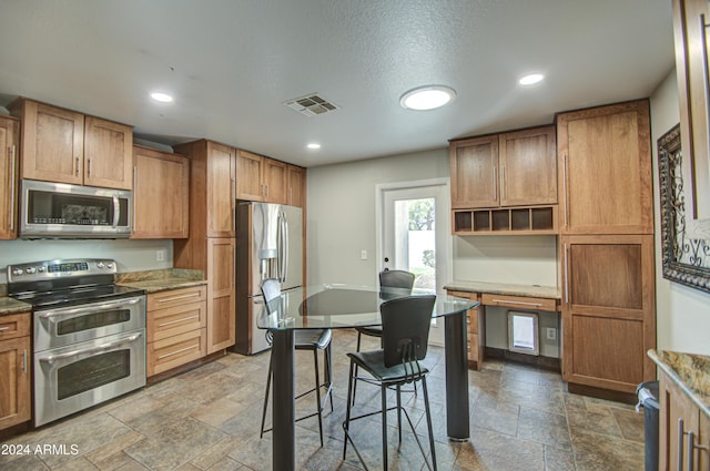 kitchen with a textured ceiling, appliances with stainless steel finishes, and dark stone counters