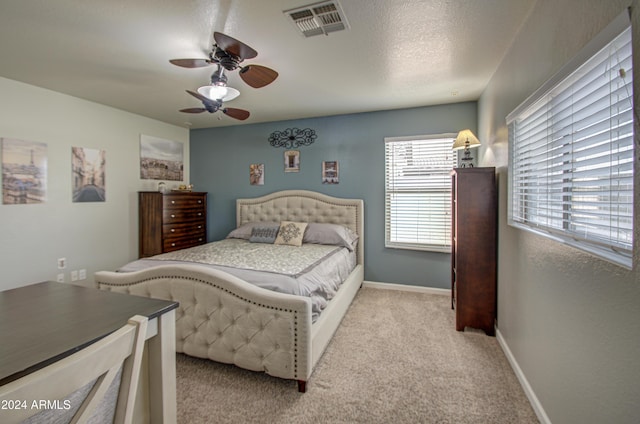 bedroom with ceiling fan, light colored carpet, and a textured ceiling