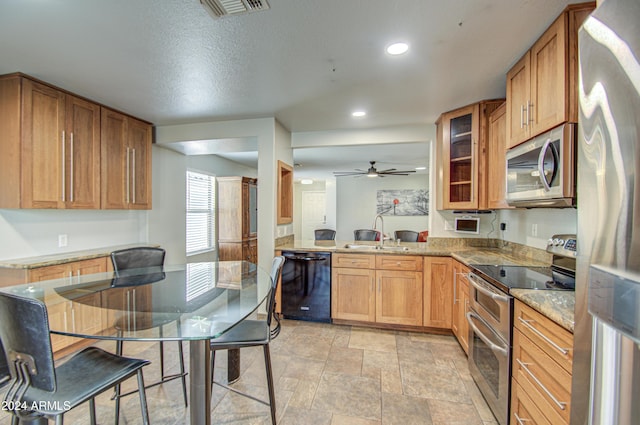 kitchen featuring light stone countertops, a textured ceiling, stainless steel appliances, ceiling fan, and sink