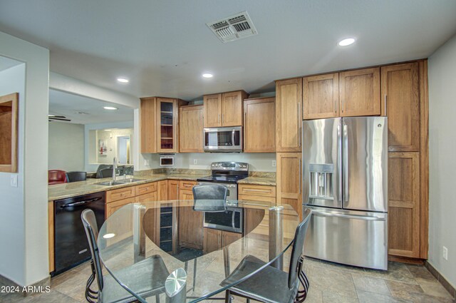 kitchen with light stone counters, kitchen peninsula, sink, and appliances with stainless steel finishes