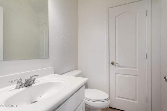 half bathroom featuring toilet, a textured wall, and vanity