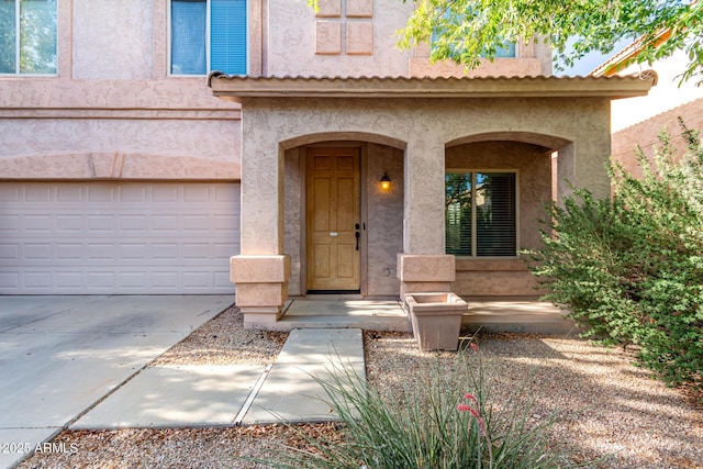 view of exterior entry with concrete driveway, an attached garage, and stucco siding