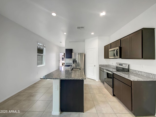 35337 W San Alvarez Ave, Maricopa, AZ 85138 - kitchen with appliances with stainless steel finishes, dark brown cabinetry, a sink, a kitchen island with sink, and light tile patterned floors