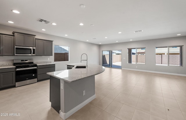 kitchen with light stone counters, recessed lighting, appliances with stainless steel finishes, a sink, and an island with sink