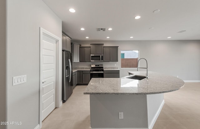 kitchen with stainless steel appliances, visible vents, a sink, an island with sink, and light stone countertops