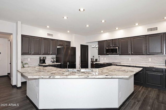 kitchen with freestanding refrigerator, stainless steel microwave, a large island with sink, tasteful backsplash, and dark wood-style floors