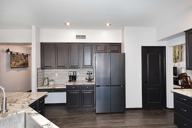 kitchen with freestanding refrigerator, dark wood-style floors, tasteful backsplash, and light stone counters