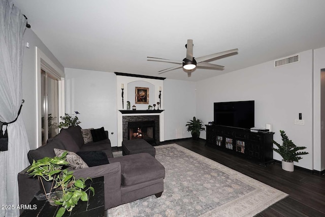 living room featuring a lit fireplace, ceiling fan, and dark wood-type flooring