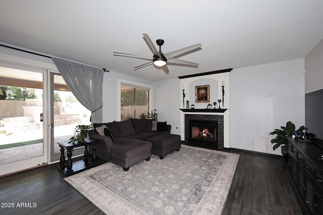 living room with dark wood-type flooring, a ceiling fan, and a fireplace with flush hearth
