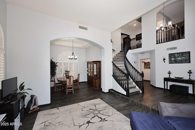 living area with a chandelier, wood finished floors, arched walkways, stairs, and a high ceiling