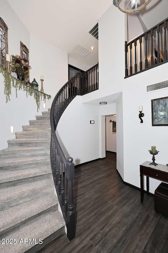 staircase with wood finished floors, a towering ceiling, baseboards, and recessed lighting