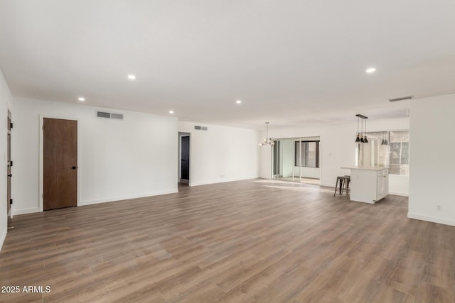 unfurnished living room featuring visible vents, a chandelier, wood finished floors, and recessed lighting