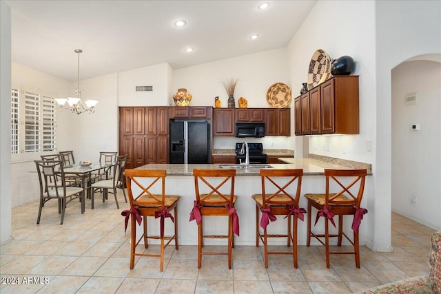 kitchen featuring a breakfast bar, black appliances, kitchen peninsula, decorative light fixtures, and a notable chandelier