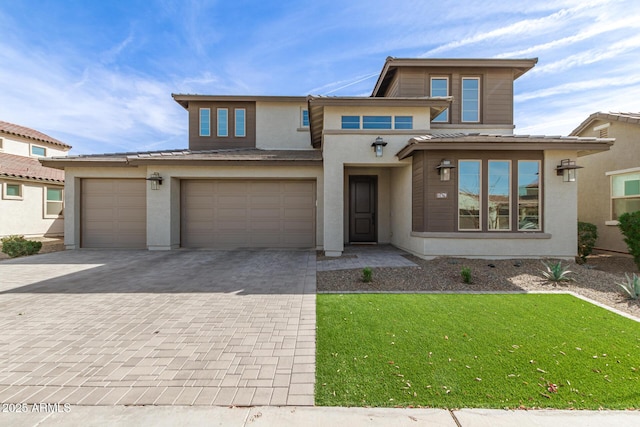 prairie-style home featuring stucco siding, decorative driveway, and a front yard