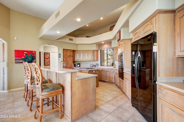 kitchen with black appliances, a breakfast bar, an island with sink, and light brown cabinets