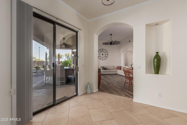 interior space with ceiling fan, crown molding, arched walkways, light tile patterned floors, and baseboards