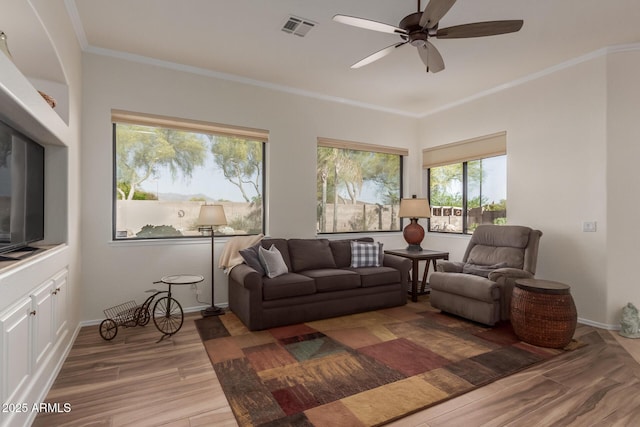 living area with visible vents, crown molding, wood finished floors, baseboards, and ceiling fan