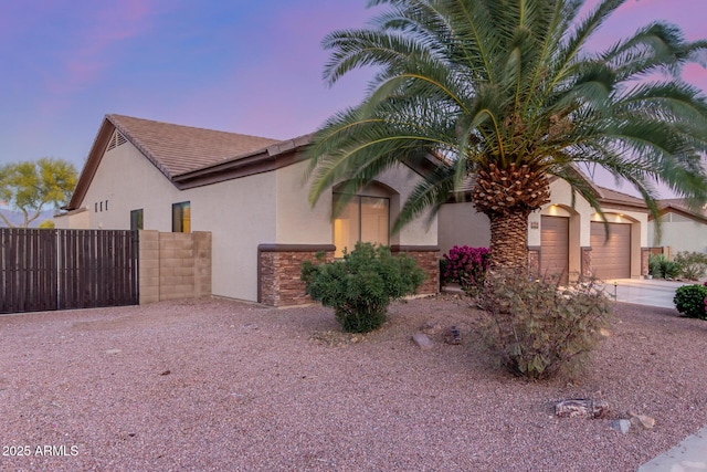 view of front of house with fence, concrete driveway, an attached garage, stone siding, and stucco siding